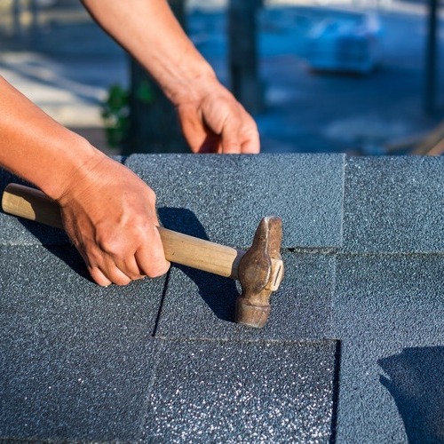 close-up of a roofer nailing down gray roofing shingles