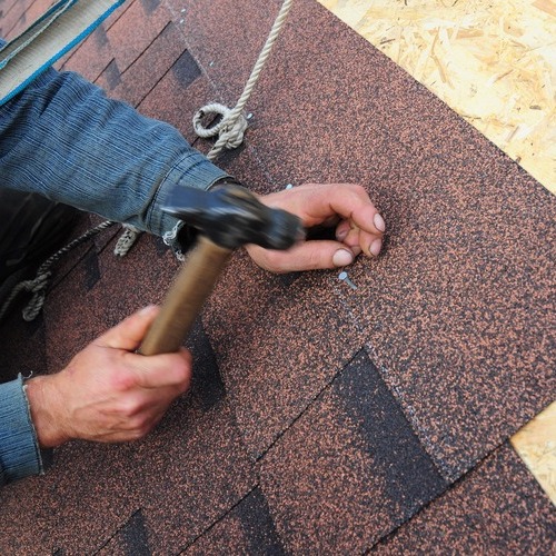 close-up of a roofer installing asphalt shingle roofing