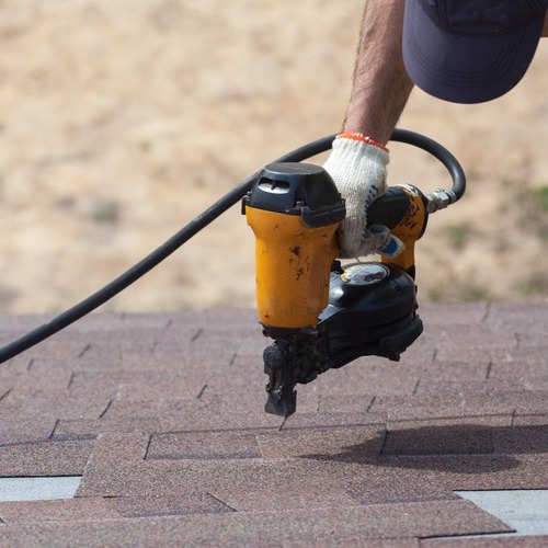 close-up of a roofer installing shingles with a nailgun